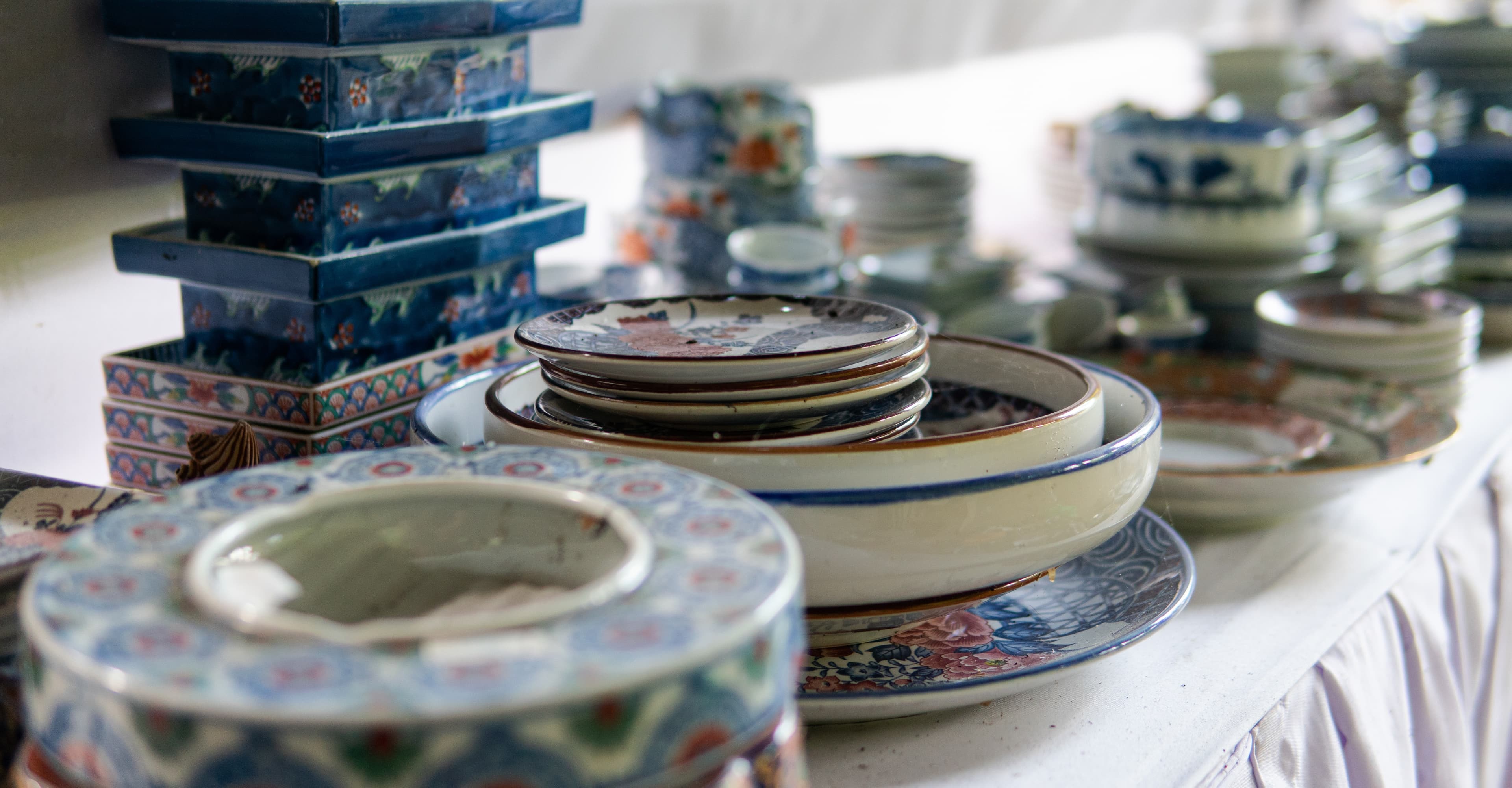 A long table of vintage dishware and antiques inside a bright estate sale space.