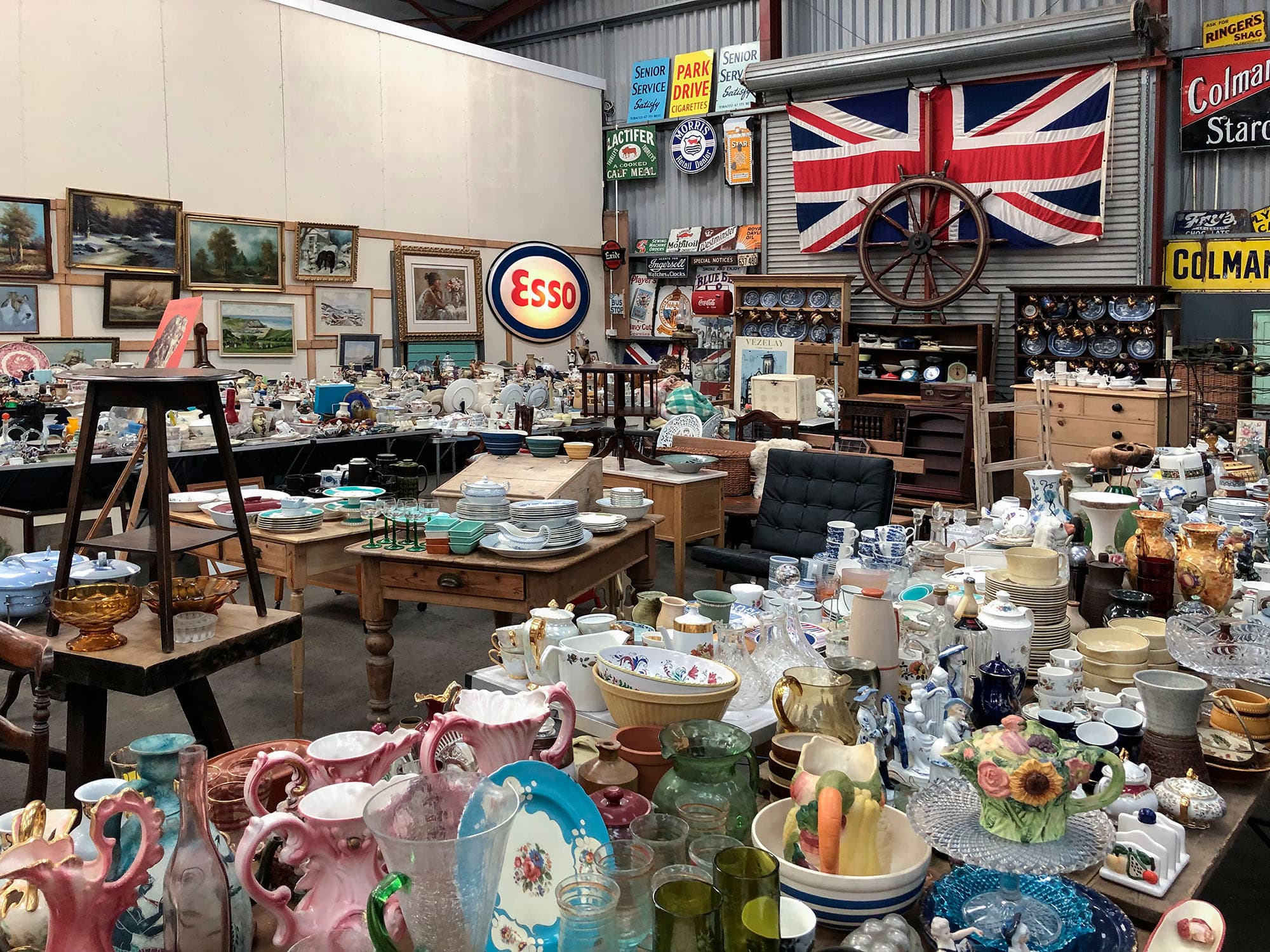 A busy estate sale floor filled with antiques, dishware, and collector finds.